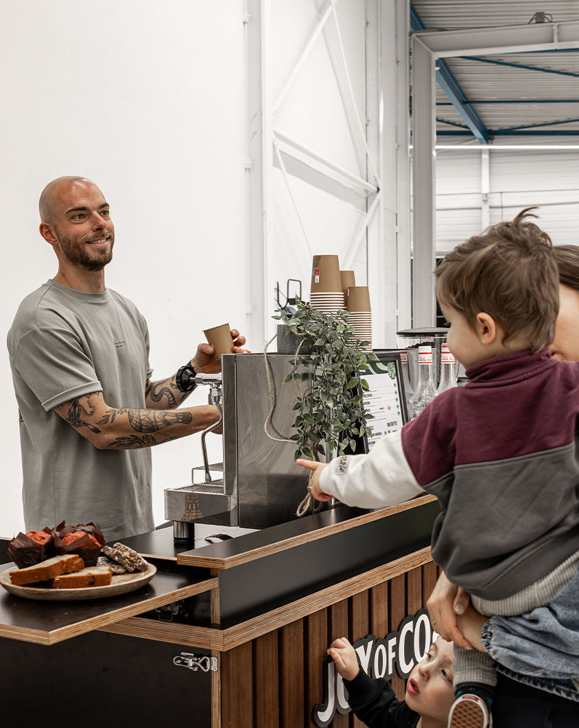 Barista schenkt koffie voor bezoekers bij de mobiele koffiebar van Joy of Coffee