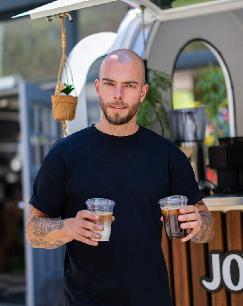 Joy of Coffee barista met twee ijskoude koffies: iced latte en iced americano bij de koffietrailer